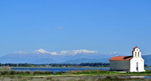 Scenic view of building by mountains against clear blue sky