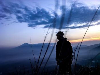 Rear view of silhouette man standing on mountain against sky