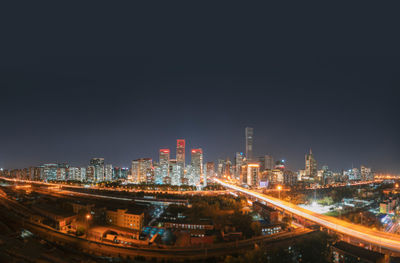 Illuminated modern buildings in city against sky at night