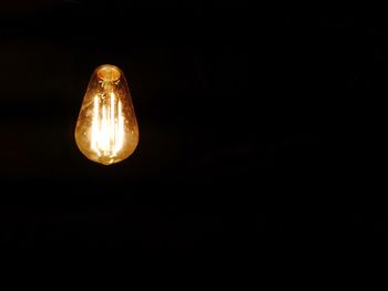 Low angle view of illuminated light bulb against black background