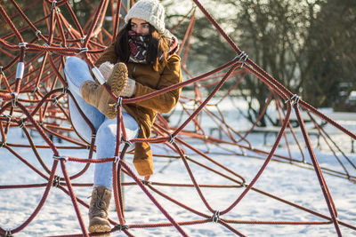 Full length of woman resting on ropes at snow covered park