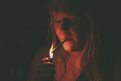 Close-up of woman lightning cigarette in darkroom