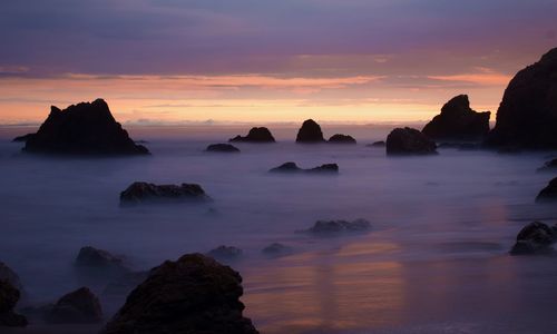 Rocks in sea against sky during sunset