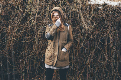 Portrait of young woman covering face with hair against dried ivy