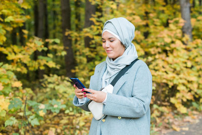 Young woman using phone while standing on plants