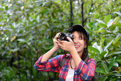 Woman photographing through camera against tree