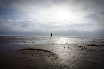 Person standing at beach against cloudy sky