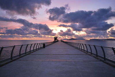 Pier over sea against cloudy sky during sunset