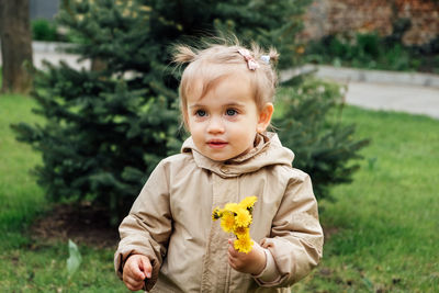 Little toddler baby girl in trench coat picking yellow dandelions in spring garden. cute baby girl