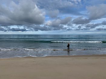 Rear view of man fishing at beach against sky