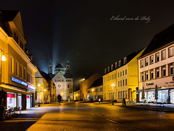 Illuminated street amidst buildings in city at night