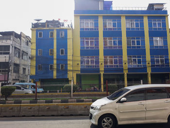 Cars on road by building in city against sky