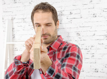 Carpenter examining wood while working against wall in workshop