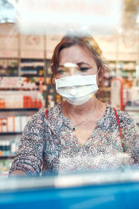 Woman shopping at pharmacy, buying medicines, wearing face mask to cover mouth and nose