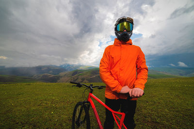 Cyclist in an orange bright jacket and a protective helmet stands and holds a bicycle in the