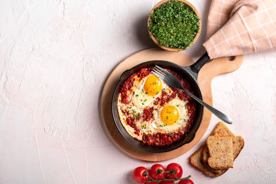 Flat lay image of shakshouka in a pan on a light coloured background close up