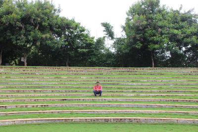 Man sitting on steps in park against sky