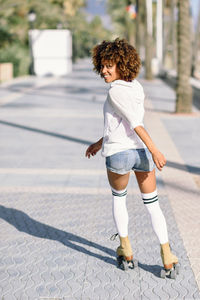 Full length of young woman roller skating on street in city during sunny days