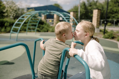 Sibling kissing at carousel in park on sunny day