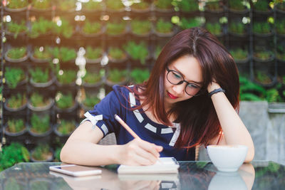 Woman with hand in hair writing while sitting at table