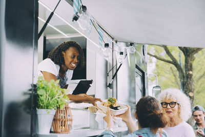 Female owner giving indian food to smiling customers in city