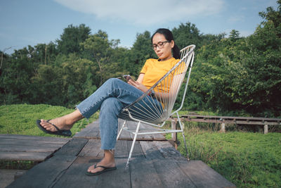 Young woman sitting on wood against trees