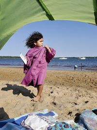 A curly-haired preschooler on the beach in her grandmother's pink cover-up shirt.