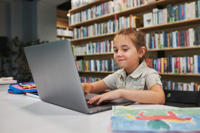 Little student having video class remotely with her teacher on laptop sitting in after school club