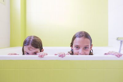 Portrait of siblings taking bath in tub at bathroom