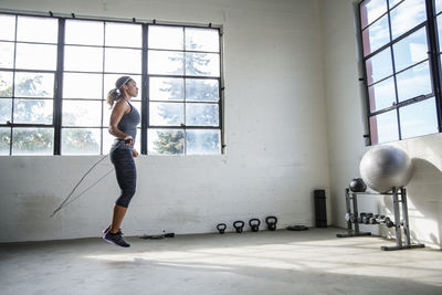 Side view of female athlete skipping with jumping rope in gym