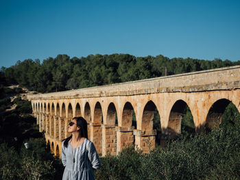 Woman standing by bridge against clear blue sky