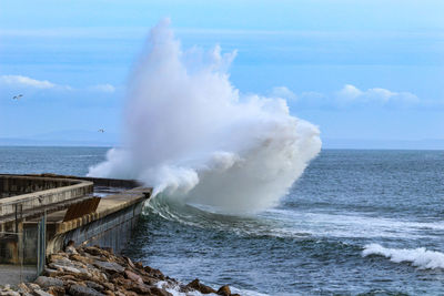 Waves splashing on rocks against sky