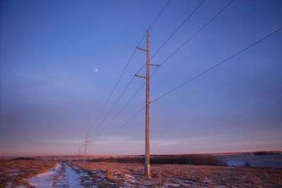 Low angle view of electricity poles on field against sky at dusk