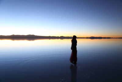 Silhouette man standing in lake against sky during sunset