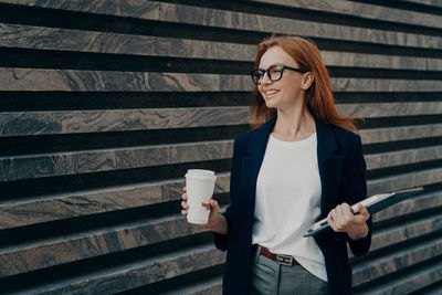 Portrait of young woman standing against wall