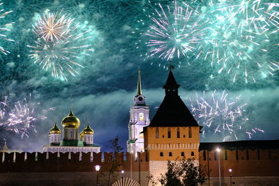 Firework display over illuminated building against sky at night