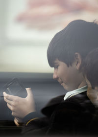 Close up portrait of kids with school uniform through car window glass playing with smartphone.