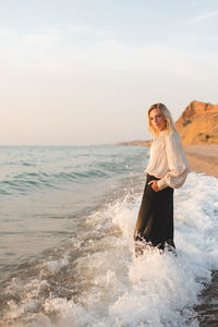 Elegant young woman wear stylish black pants and shirt standing in sea water over coast line outdoor