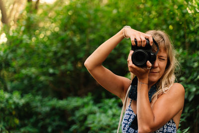 Blonde woman taking a picture standing in a park