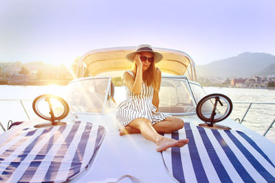 Full length of young woman sitting on boat in lake against sky