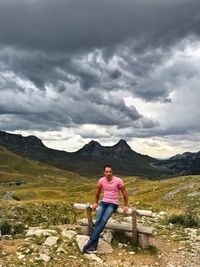 Full length of man sitting on bench against mountain