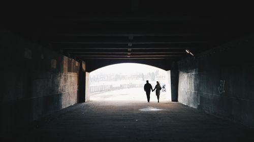 Rear view of silhouette couple walking in tunnel