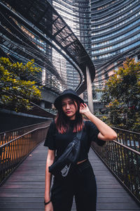 Portrait of young woman standing on footbridge in city