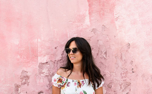 Portrait of young woman wearing sunglasses standing against pink wall