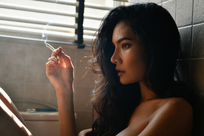 Thoughtful seductive woman smoking cigarette in bathroom