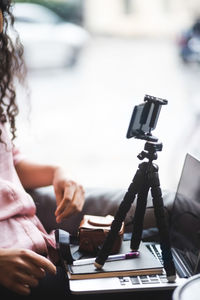 Midsection of young female influencer vlogging through mobile phone on tripod by window at creative office