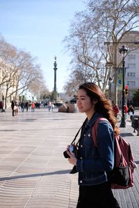 Side view of young woman standing on footpath in city