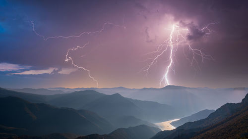 Low angle view of lightning over mountains against sky