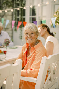 Portrait of smiling elderly woman sitting on chair at back yard