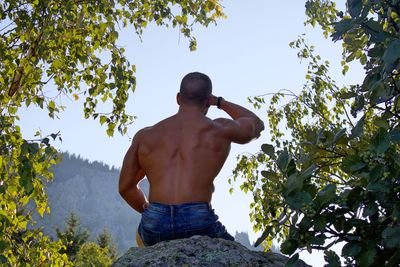 Rear view of shirtless man looking at tree against sky